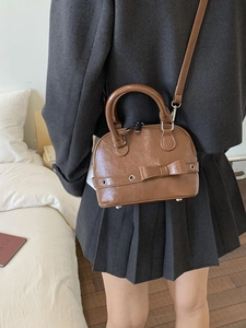 Classic brown shell bag with bow detail and glossy finish shown as a crossbody wear