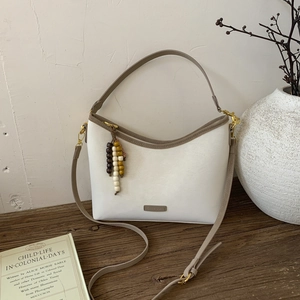 Detail of a minimalist cream leather crossbody bag with wooden beads on a wooden table