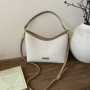 Close-up of the elegant metal brand logo on the white leather vintage bucket bag