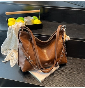 Detail of a brown leather tote bag with contrast stitching and baseball charm