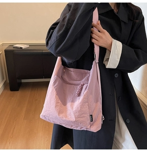 Detail of pink nylon crossbody bag with crinkle texture and SHUINUO brand label on black coat