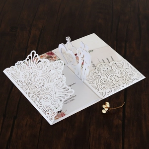 Close-up of laser-cut wedding invitation with lace patterns and pop-up heart rings