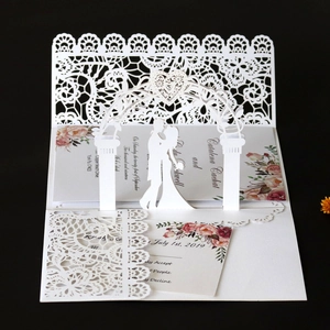 Macro view of 3D laser-cut white lace wedding invitation with floral arch and couple silhouette