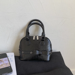 Close-up of black glossy shell handbag featuring decorative bow and silver hardware detail