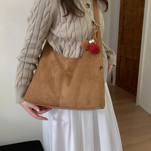 Sac hobo en daim marron avec pompons décoratifs porté par un mannequin en pull en maille