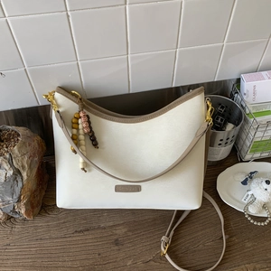 Detail of cream bucket bag with brown trim, metal logo and colorful beaded charm