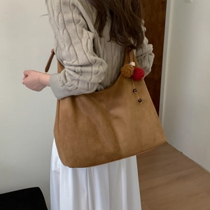Détail du sac cabas en daim marron avec pendentif à pompon décoratif et large bandoulière