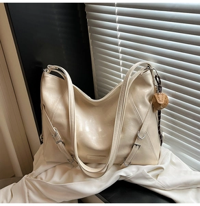 Detail of creamy white tote bag featuring side buckle decor and brown elephant charm