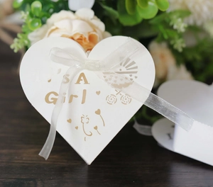 Detailed view of a white heart-shaped candy box with golden It's a Girl text and bow