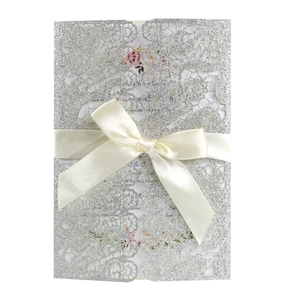 Detail of silver glitter laser-cut invitation with cream satin bow and floral insert