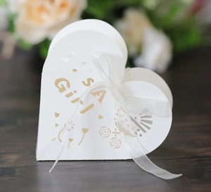 Macro shot of heart-shaped It's a Girl favor box with white ribbon and gold lettering