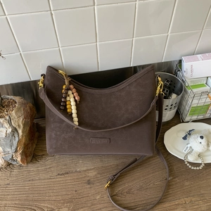 Detail of vintage brown suede shoulder bag with beaded charm on wooden tabletop