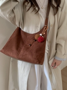 Sac hobo marron en daim avec pendentif à pompons porté par un mannequin chic