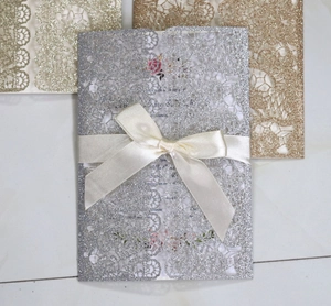 Detail of silver glitter laser-cut floral wedding invitation with cream satin ribbon bow