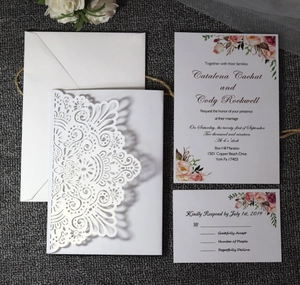 Detailed laser cut white floral wedding invitation set with elegant RSVP card on textured base