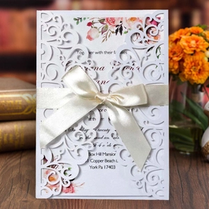 Elegant laser cut wedding invitation with white lace pattern and cream satin bow detail