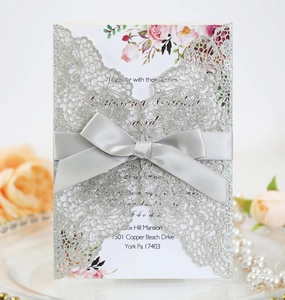 Close-up of laser-cut floral lace invitation with silver glitter finish and grey satin bow