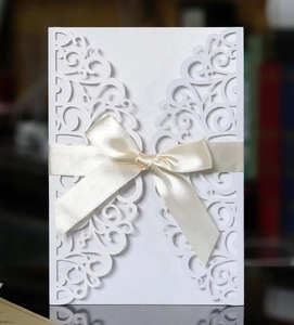 Detailed laser-cut vine patterns on white invitation card with a gold satin ribbon bow