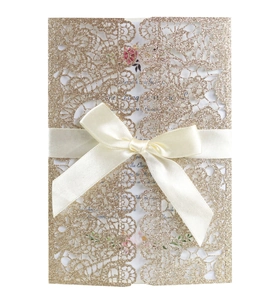 Detail of laser-cut lace wedding invitation with gold glitter and white satin bow