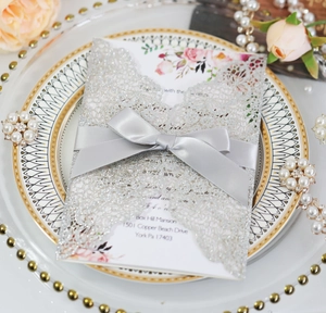 Macro shot of silver laser-cut wedding invitation with glitter finish and satin bow