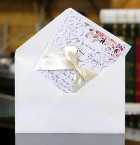 Detail of laser-cut floral wedding invitation with cream ribbon and white envelope