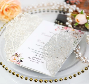 Macro shot of laser-cut wedding invitation with silver glitter lace and floral insert