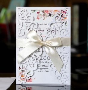 Detail of laser cut wedding invitation with elegant floral patterns and beige silk ribbon