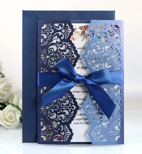 Detail of laser-cut wedding invitation with navy blue ribbon and hollow floral patterns