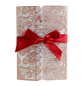 Detail of rose gold laser cut lace wedding invitation with a red satin bow accent