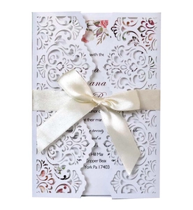 Elegant white laser-cut wedding invitation with beige ribbon bow and pink floral insert card