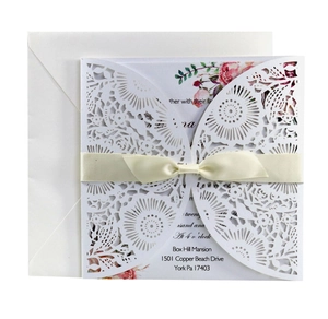 Intricate laser-cut wedding invitation set with floral cover and elegant ribbon bow