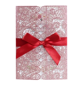 Detail view of pink glitter laser-cut lace wedding invitation with a red satin bow ribbon