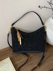 Vintage black faux suede bucket bag with colorful wooden bead tassel on a wooden desk
