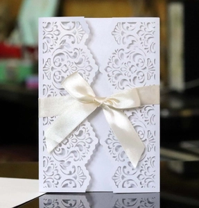 Close-up of laser-cut floral wedding invitation with ivory satin ribbon bow