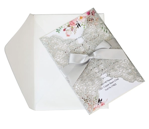 Detail of silver laser-cut wedding invitation with grey silk bow and floral insert