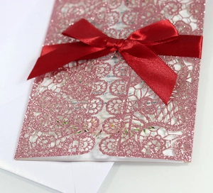 Macro detail of laser-cut glitter wedding invitation with elegant red satin ribbon bow