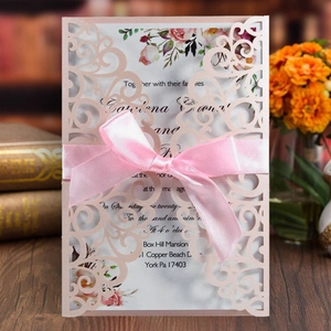 Detail of laser cut lace wedding invitation with pink ribbon bow and floral card
