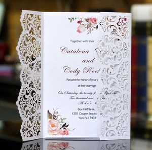 Detail of laser-cut white wedding invitation with intricate floral vine hollow design