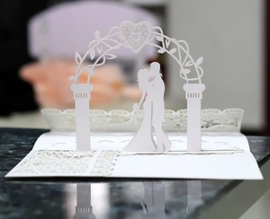 Macro detail of 3D laser-cut wedding card featuring a romantic couple under heart arch