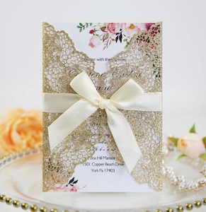 Detail of laser-cut gold glitter wedding invitation with satin bow and floral print