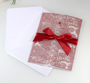 Detail of pink glitter laser-cut invitation card with a red satin bow and white envelope