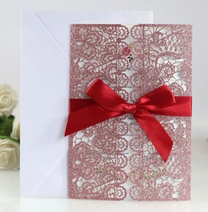 Detail of rose gold laser-cut wedding invitation with red ribbon and white envelope
