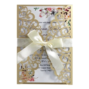 Macro detail of laser-cut gold wedding invitation with navy floral insert and ribbon