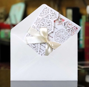 Elegant laser-cut white wedding invitation set with silk bow and matching envelope