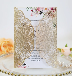 Detail of laser-cut gold wedding invitation with floral insert on elegant pearl plate