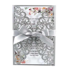 Detail of silver laser-cut lace wedding invitation with satin ribbon and floral insert