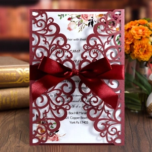 Detail of laser-cut burgundy wedding invitation with elegant satin bow and floral insert