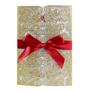 Detailed laser-cut gold glitter invitation with elegant red satin bow and floral inner card