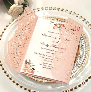 Detail of pink laser-cut wedding invitation sleeve with floral inner card on glass tray