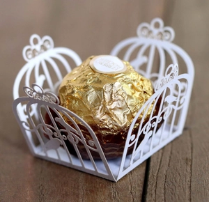 Detailed close-up of a white laser-cut wedding candy box with an intricate hollow birdcage pattern
